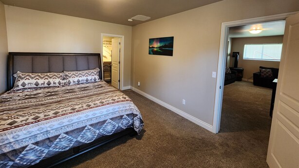 A bedroom with a bed, a door leading to another room, a painting on the wall, and a ceiling light.