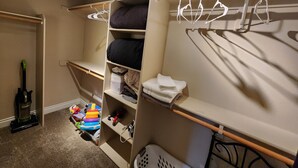 A compact storage closet with shelves, hanging space, and a vacuum cleaner.