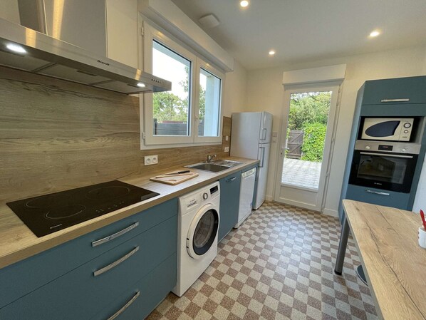 A compact kitchen with a built-in washing machine, a microwave, and a stove. - Renovated Beachside House, 4BR, Sleeps 10, Garden, BBQ, Free WiFi, Parking (Saint-Jean-de-Monts)
