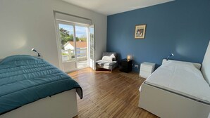 Ein Schlafzimmer mit zwei Betten, einer Schiebetür zum Außenbereich, einem kleinen Nachttisch mit Lampe und einem gerahmten Bild an der Wand.