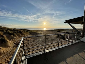 A beach with a metal staircase leading down to the sand, a wooden walkway, and a clear sky with the sun setting in the distance. - Renovated Beachside House, 4BR, Sleeps 10, Garden, BBQ, Free WiFi, Parking (Saint-Jean-de-Monts)