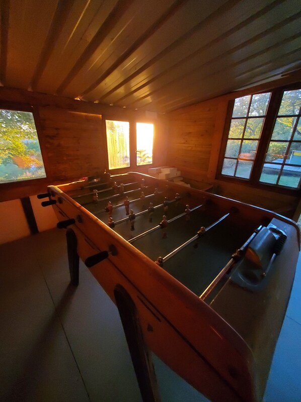 A room with a foosball table, wooden walls, and large windows.