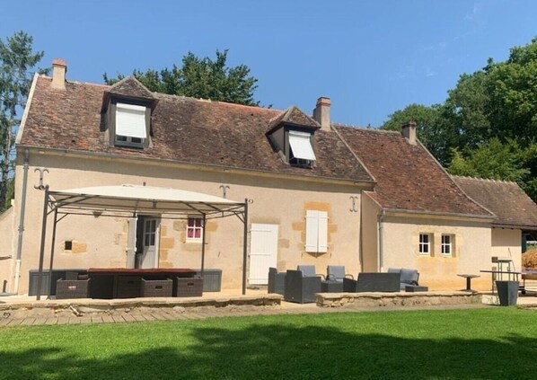 Une maison à deux étages avec un patio couvert, un petit jardin et un toit en briques.