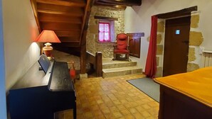 Una habitación acogedora con techo de madera, piso de baldosas, un escritorio con lámpara, una silla y una puerta roja.