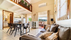 A spacious living area with a high ceiling, a dining area with modern furniture, and a balcony with a view.