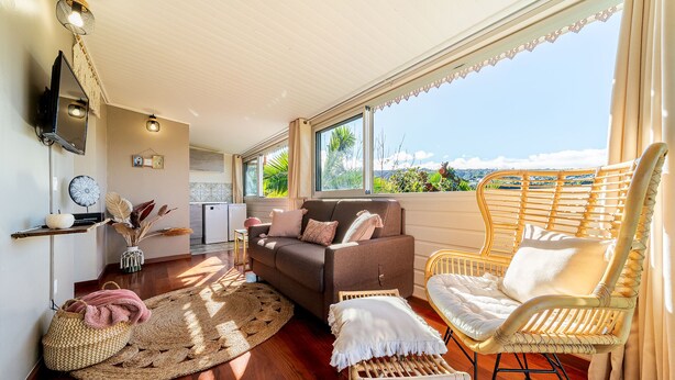 A cozy living room with a sofa, two wicker chairs, a coffee table, and a large window offering a view of the outdoors.