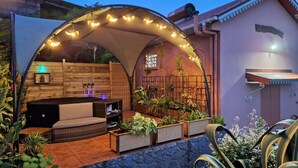 An outdoor patio with a covered seating area, planters, and a decorative arch with lights.
