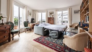 Ein Schlafzimmer mit Bett, Schreibtisch, Stuhl, Bücherregal und einem Fenster mit Vorhängen.