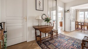 Ein Zimmer mit einem Holztisch, einer Lampe, einer Blumenvase, einem gemusterten Teppich und einem großen Spiegel.