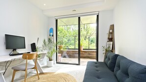 A modern living room with a grey sofa, a wooden chair, a TV, and a large sliding glass door leading to a balcony with plants. - Wandle Waters, by Veeve (London)