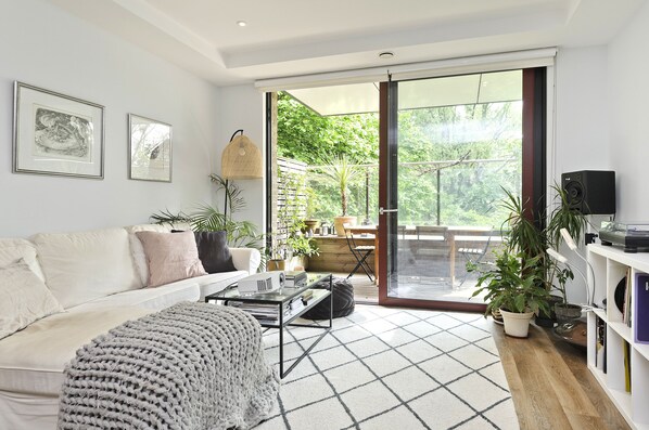 Relax in this stylish living room with a sofa, coffee table, and floor lamp, leading to an outdoor space with a deck and potted plants.