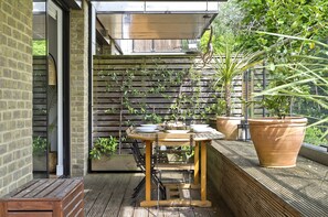 Relax in the serene patio area surrounded by lush greenery and a brick wall, perfect for enjoying a quiet moment.