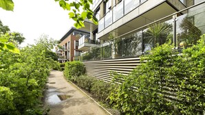 A modern building with a glass facade, a concrete pathway, and lush greenery. - Wandle Waters, by Veeve (London)