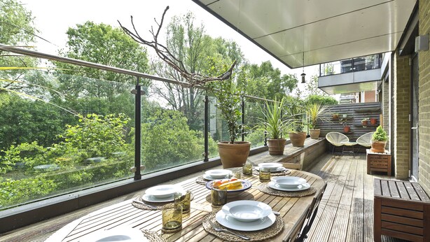 An outdoor dining area with a view of greenery, a wooden table set with plates and glasses, and potted plants. - Wandle Waters, by Veeve (London)
