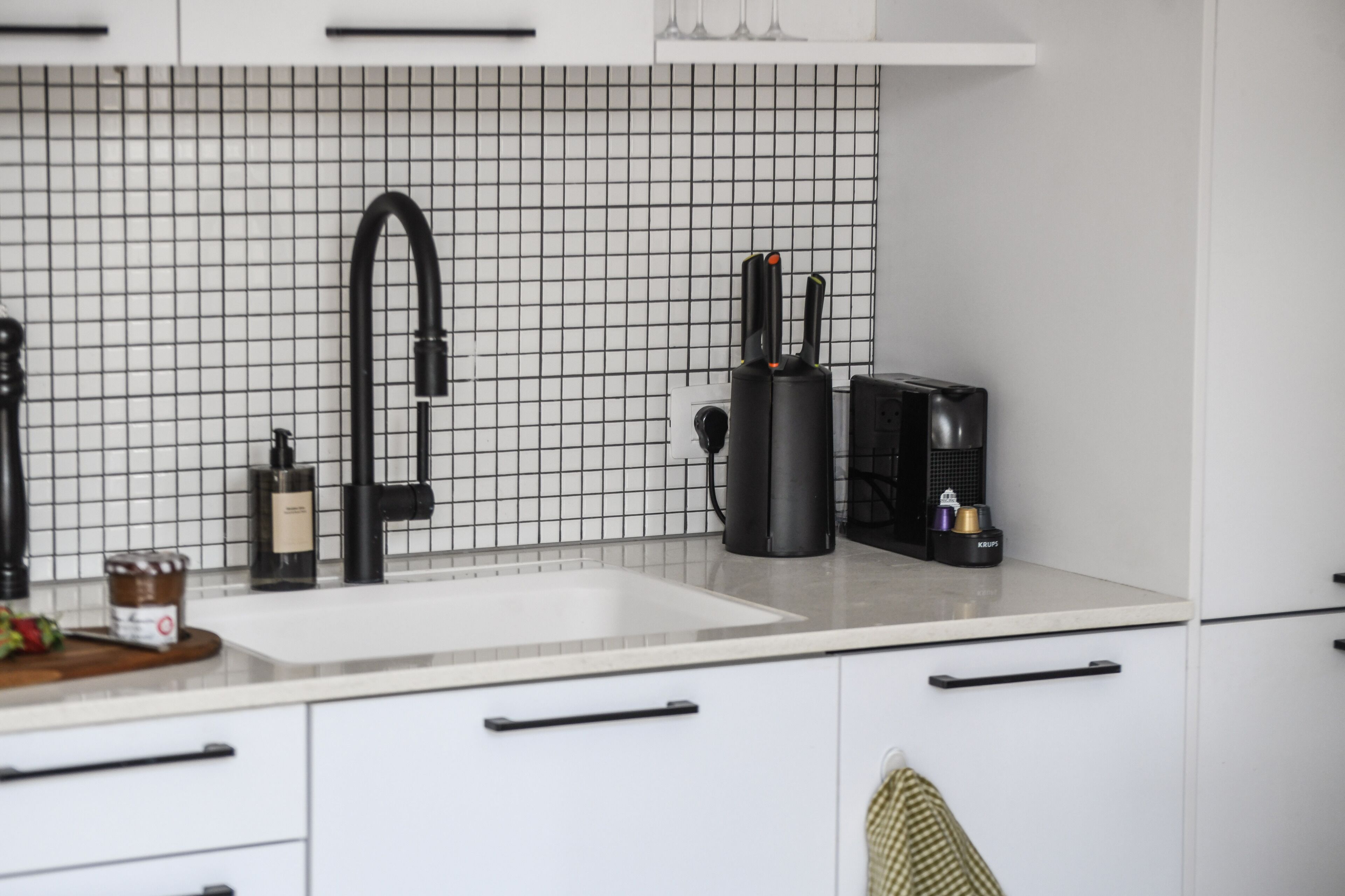 A modern kitchen with a white tiled backsplash, a black faucet, and a coffee machine.
