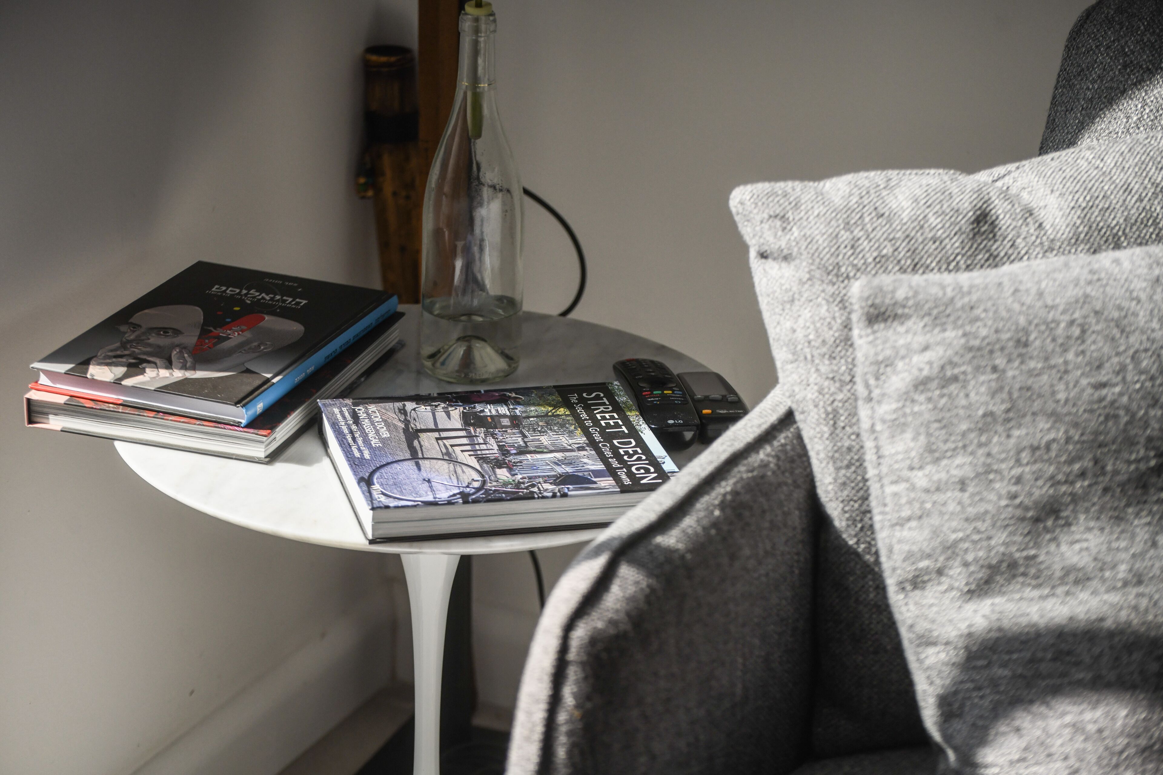 A small white table with books, a remote control, and a glass bottle.