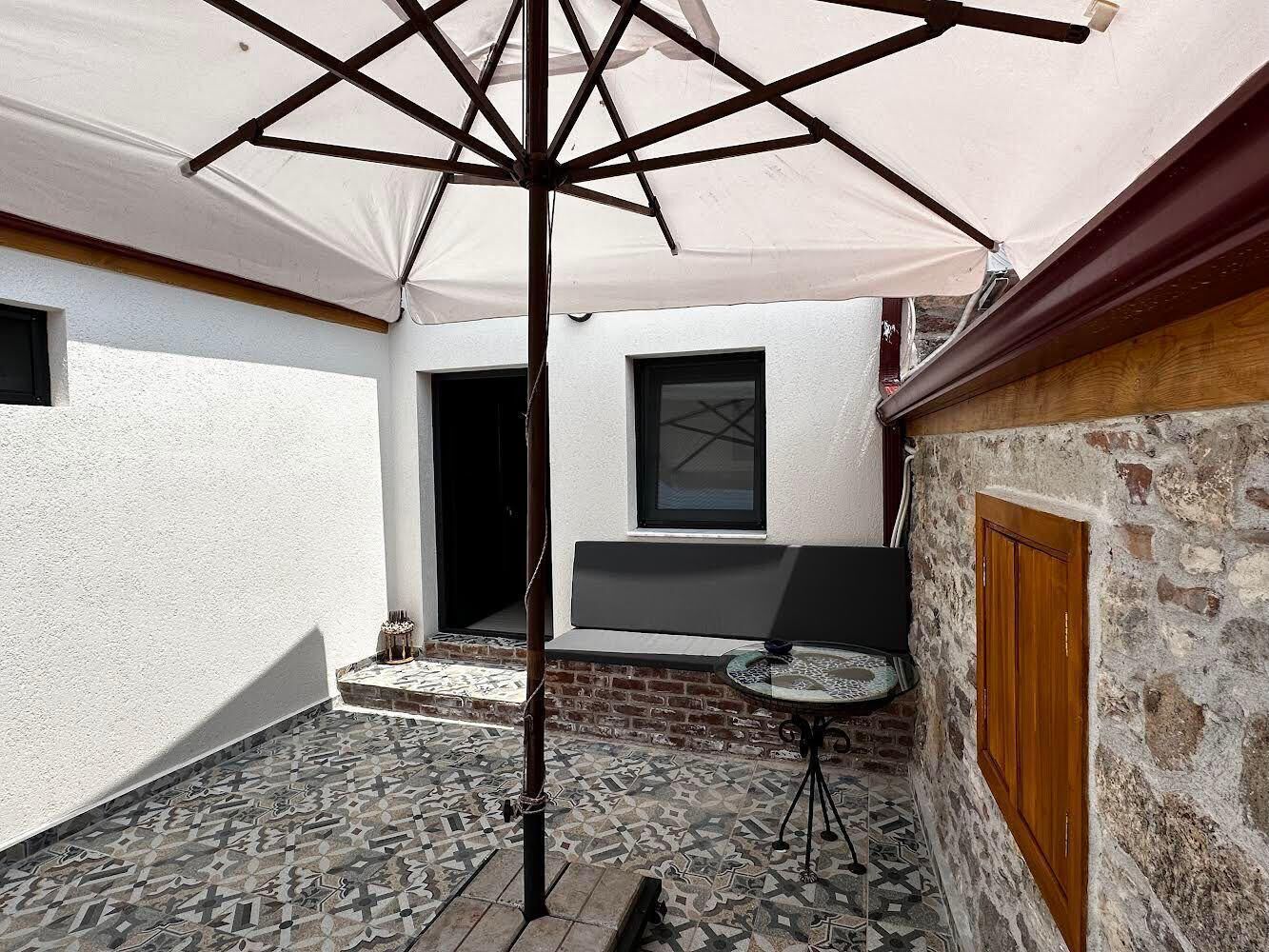 A courtyard with a tiled floor, a table, a bench, and a large umbrella.