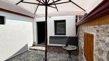 A courtyard with a tiled floor, a table, a bench, and a large umbrella.