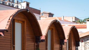 A row of wooden arched rooms with potted plants and a cobblestone path. - Vasvija Pansiyon (Ayvalik)