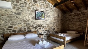 A rustic room with a stone wall, two wooden beds, a small bedside table, and a framed picture. - Vasvija Pansiyon (Ayvalik)