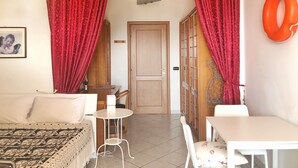 A room with a bed, a small table, a chair, a white table, and a door. - Aria - studio in center  (Tropea)