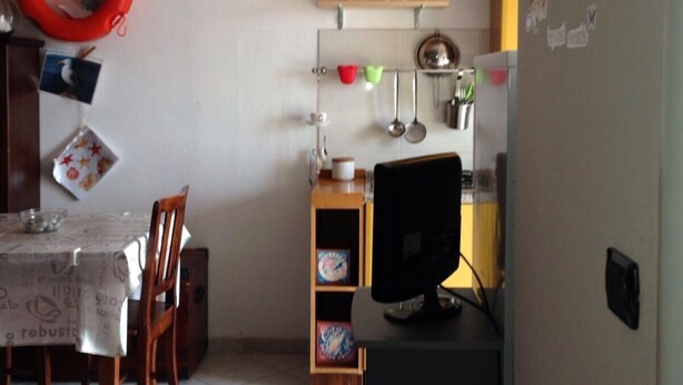 Un comedor con mesa, sillas y una zona de cocina con estantes y una computadora.