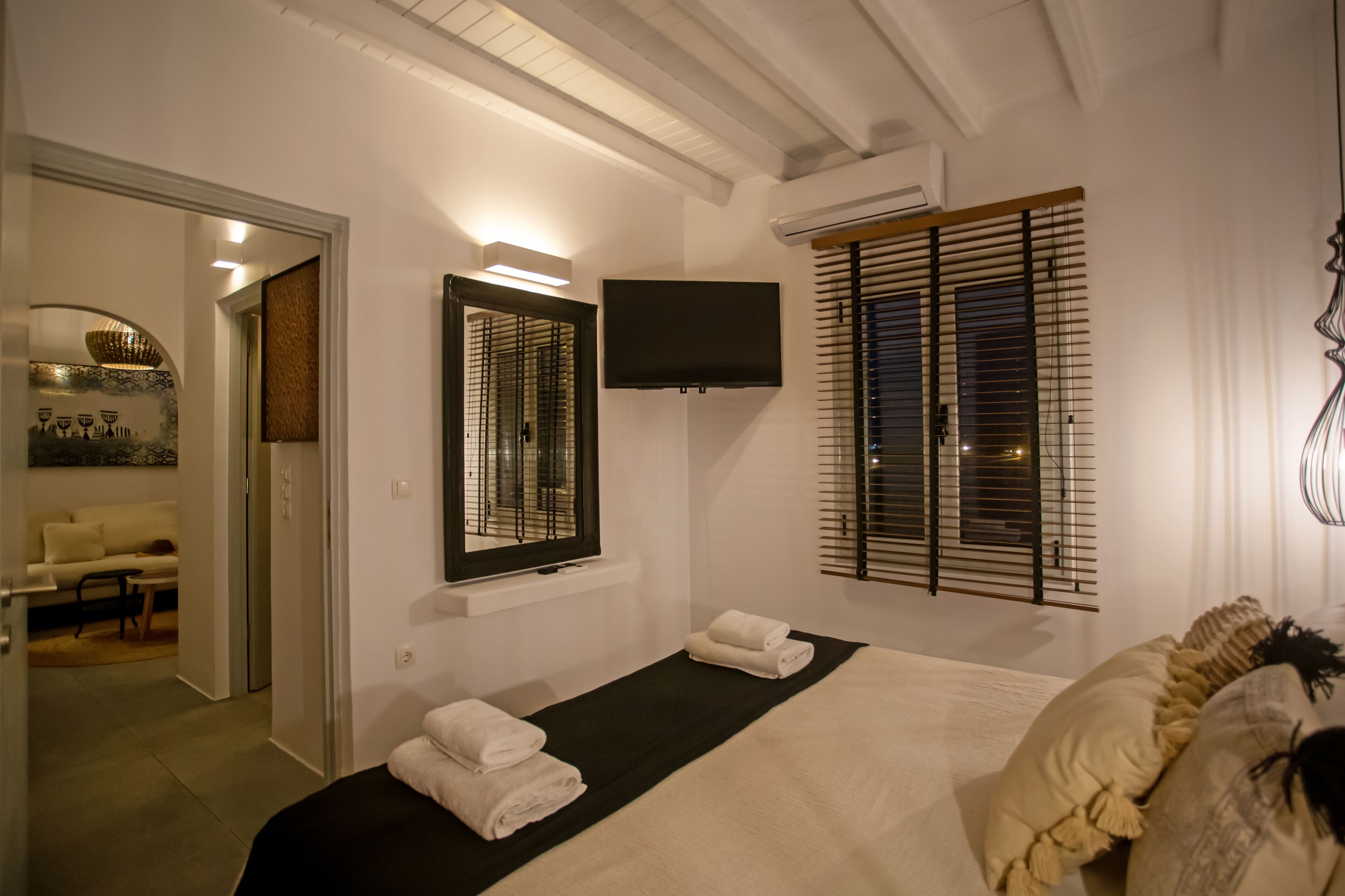 Una habitación de hotel con una cama, un televisor de pantalla plana en la pared y una ventana con persianas.