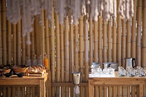 A bamboo wall with a table set for dining, featuring glassware and a kettle. - Nur Mykonian Suites (Mykonos)
