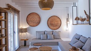 A living room with a sofa, a coffee table, and a rug. There are wall decorations and a hanging light fixture. - Nur Mykonian Suites (Mykonos)