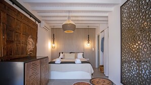 A bedroom with a bed, bedside tables, a wooden wardrobe, and a decorative wall panel. - Nur Mykonian Suites (Mykonos)