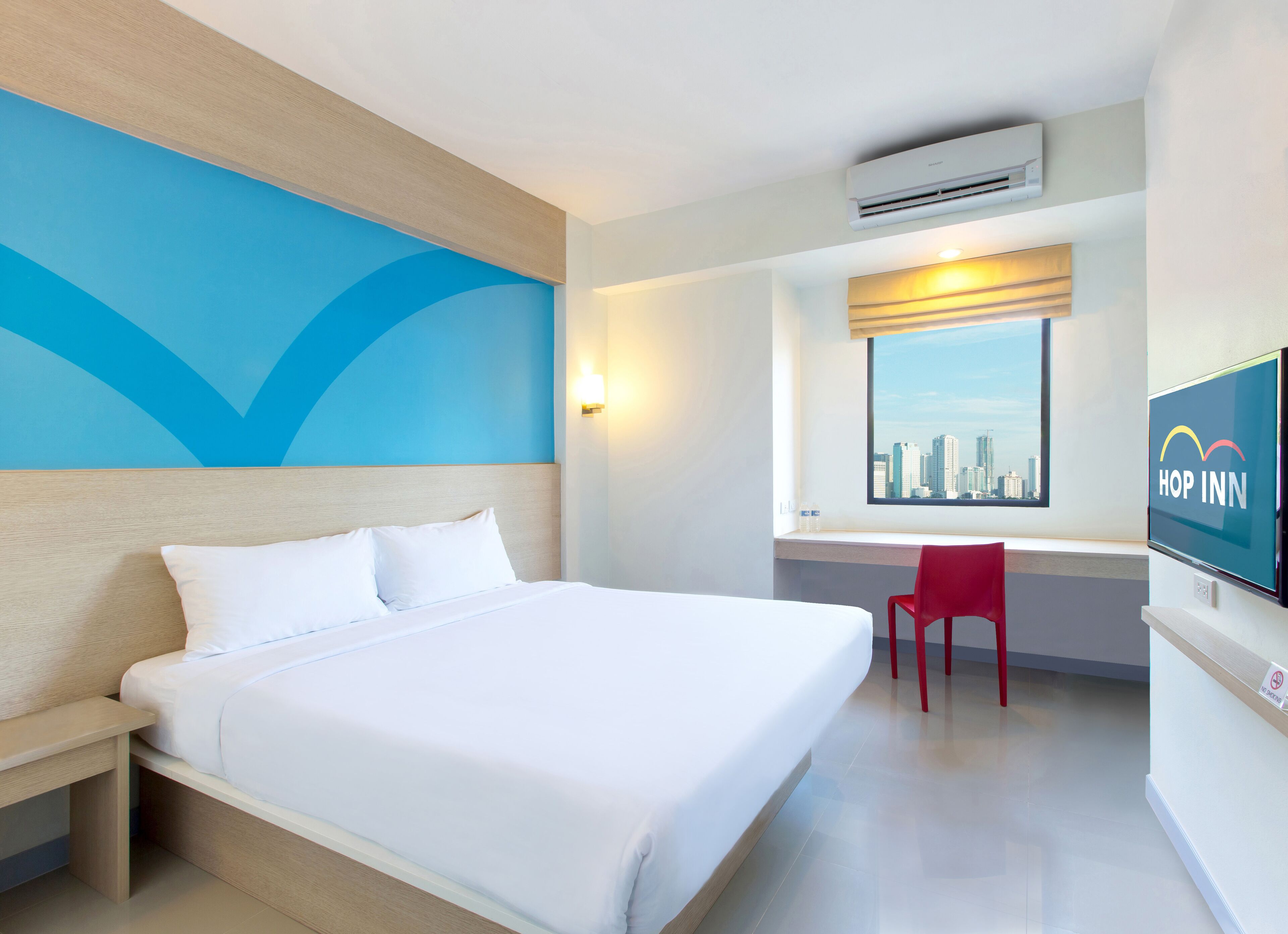 A hotel room with a bed, a desk, a chair, a TV, and a window with a city view.