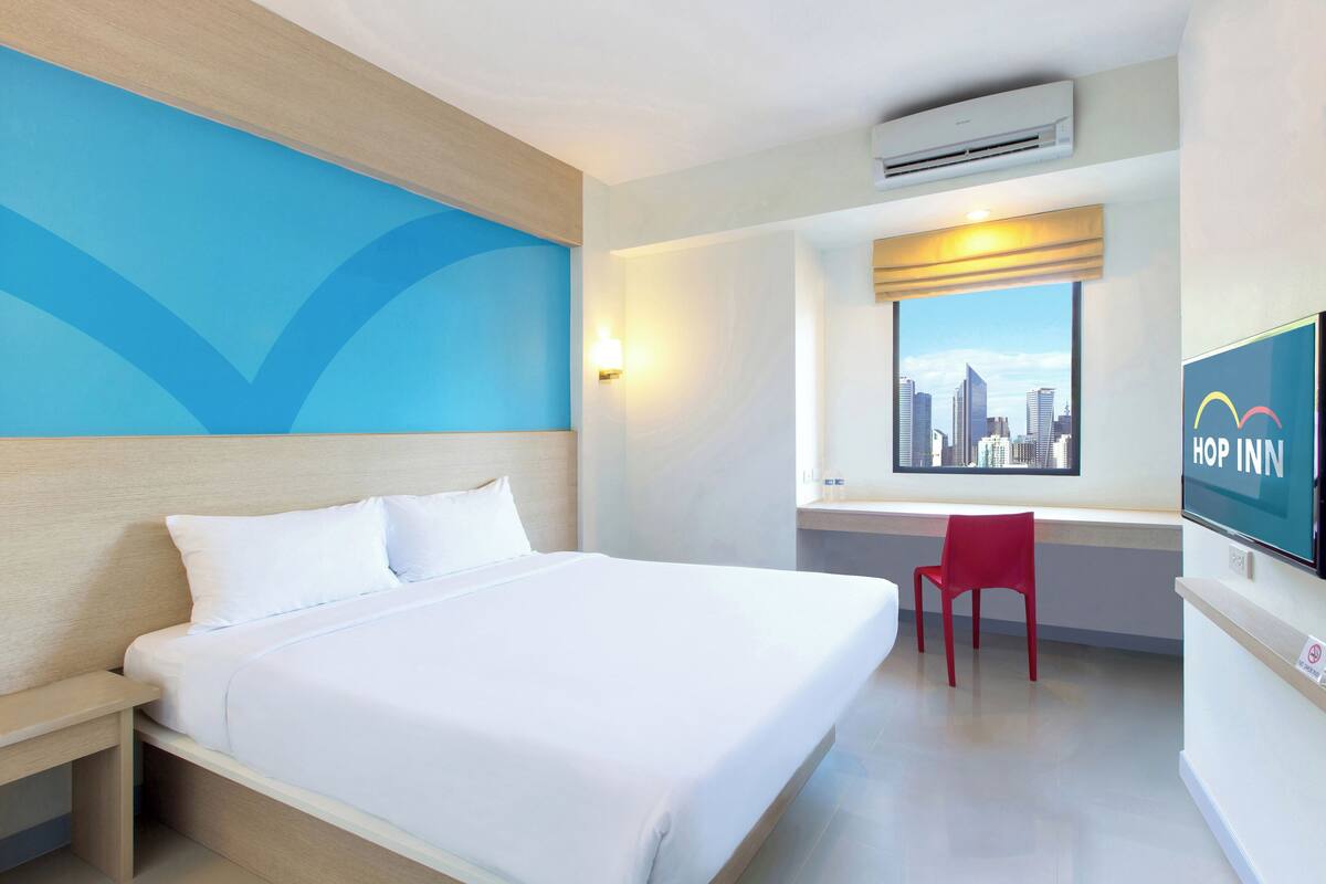 A hotel room with a bed, a desk, a chair, a TV, and a window with a city view.