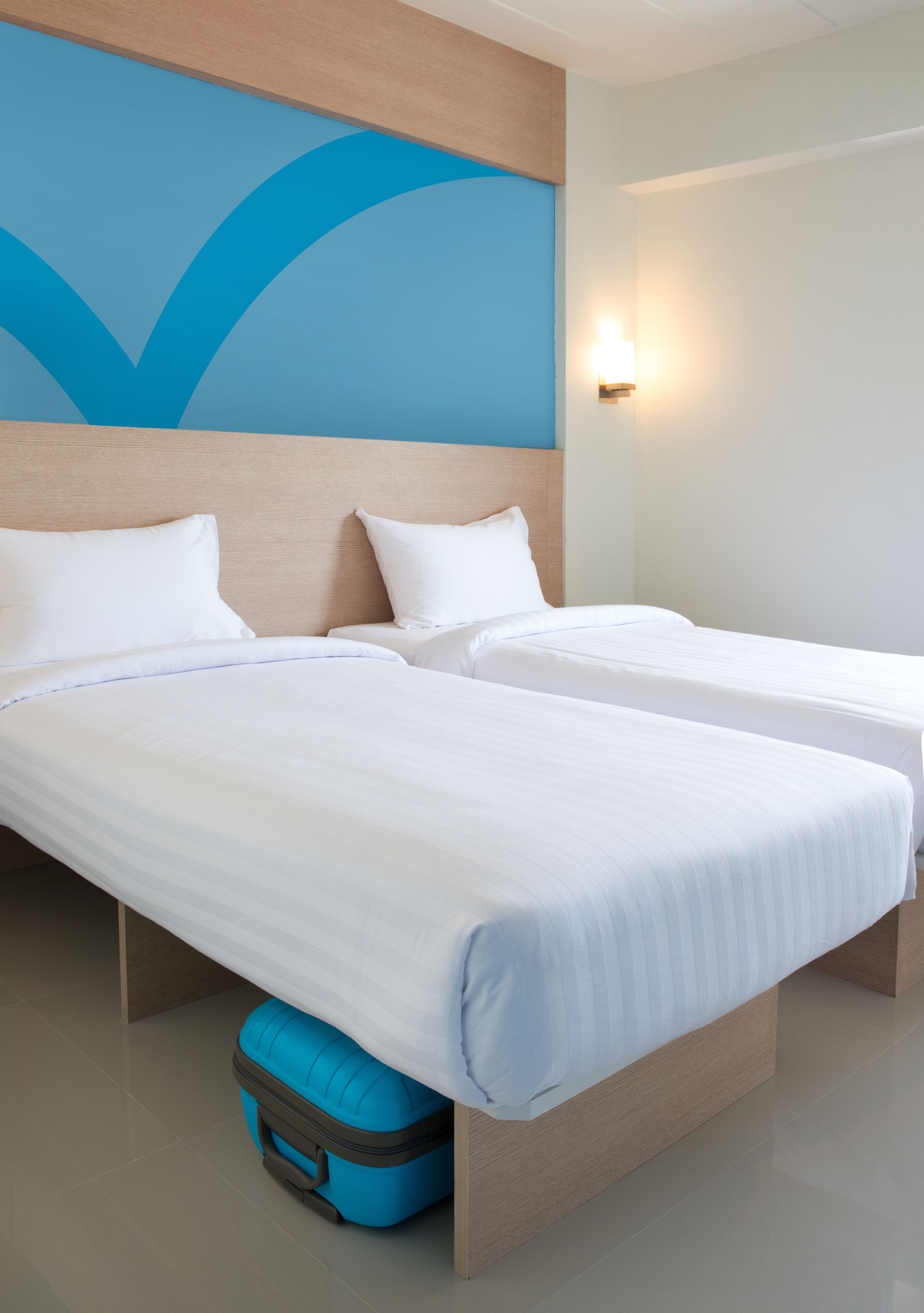 Een hotelkamer met twee bedden, een blauwe koffer en een muur met een blauw abstract ontwerp.