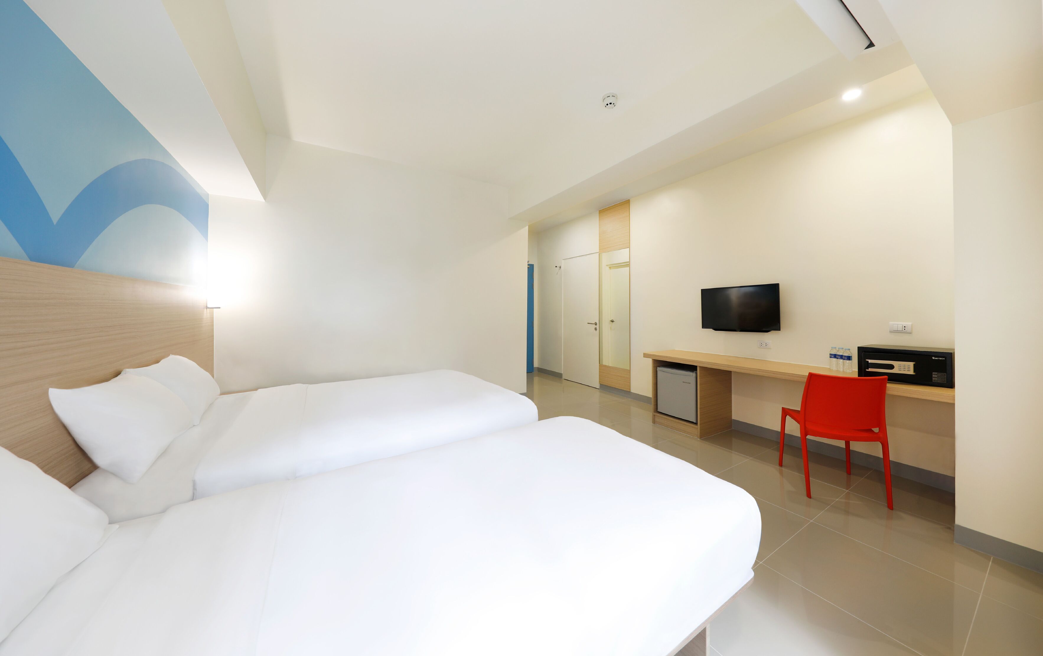 Ett hotellrum med två sängar, ett skrivbord, en röd stol, en tv och en minibar.
