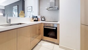 Moderni keittiö, jossa on sisäänrakennettu uuni, ruostumattomasta teräksestä valmistettu pesuallas ja suuri ikkuna työtason yläpuolella.