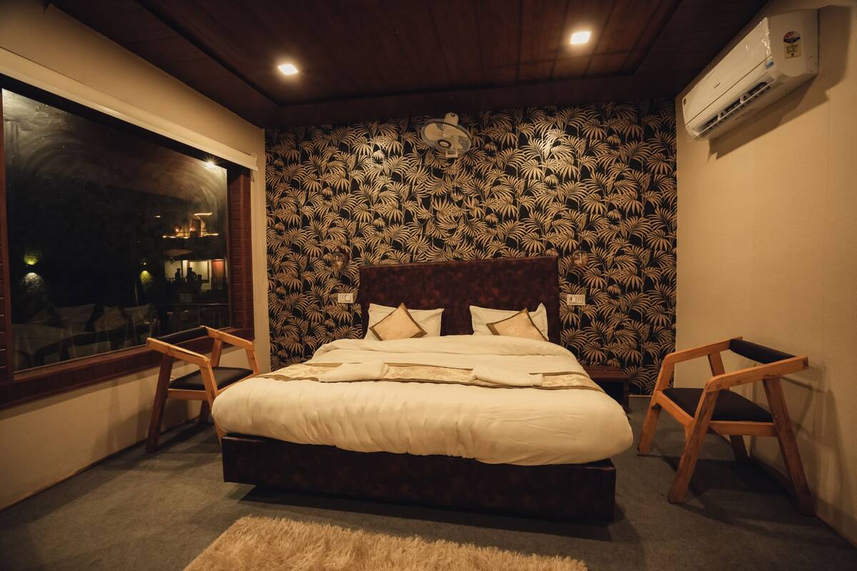 A bedroom with a large bed, two wooden chairs, a window, and a patterned wall.