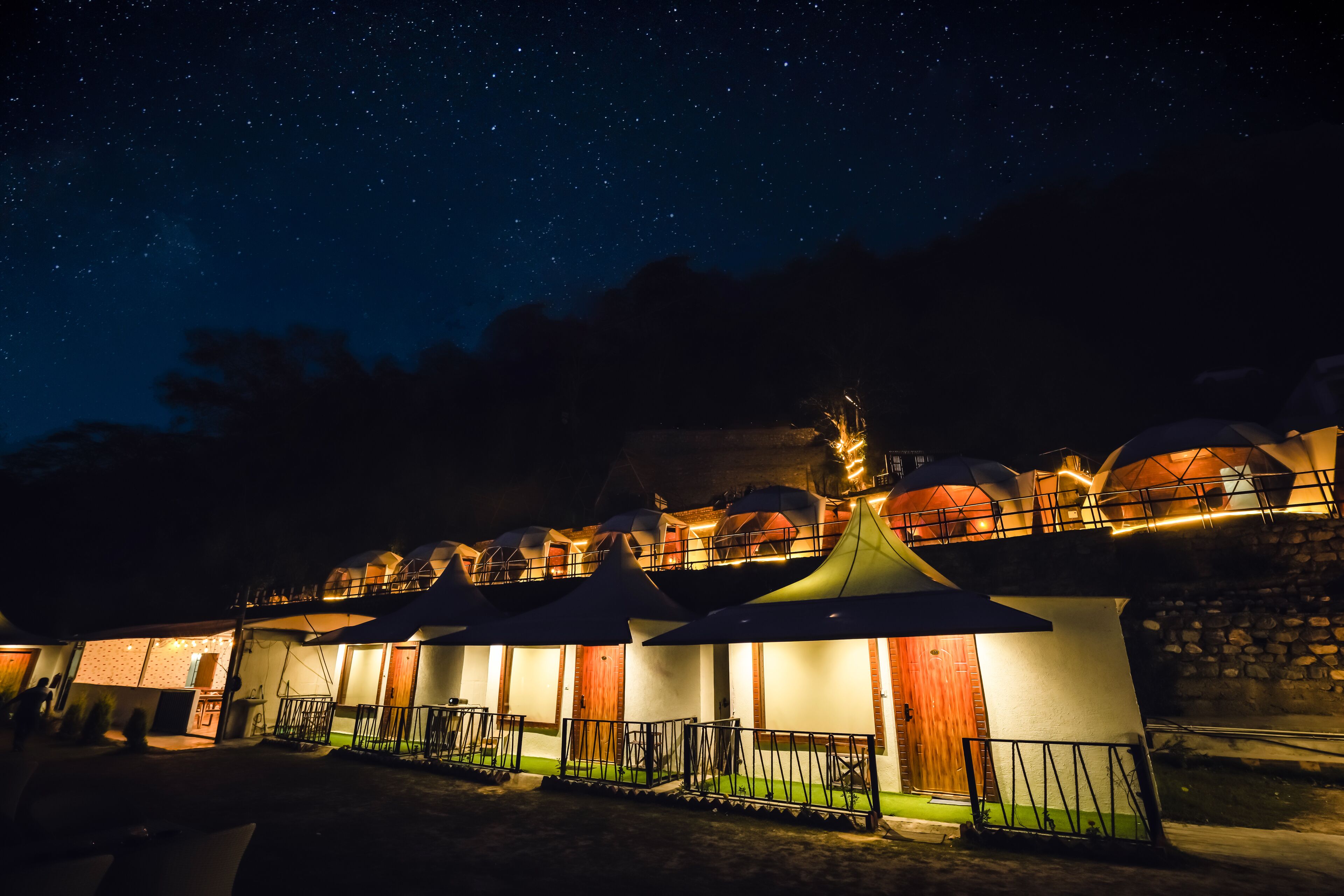 A row of dome-shaped tents with a stone wall and a wooden door, under a starry night sky.