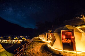 A row of dome-shaped tents with open doors, illuminated interiors, and a starry night sky. - Night in Paradise (Rishikesh)