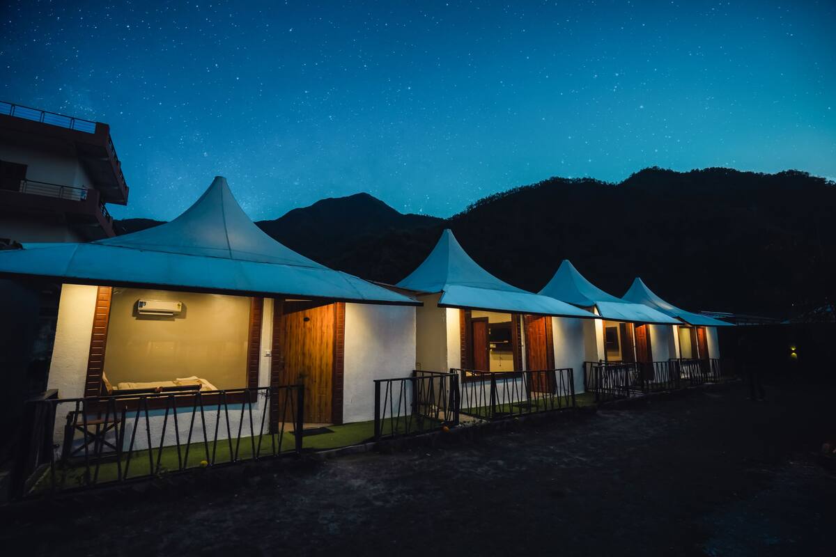 A row of tents with a view of the mountains under a starry sky.