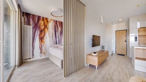 A modern bedroom with a large abstract painting, a wooden bedside table, a bed, and a built-in wardrobe. - Apartamenty Sun&Snow Modern Tower (Gdynia)