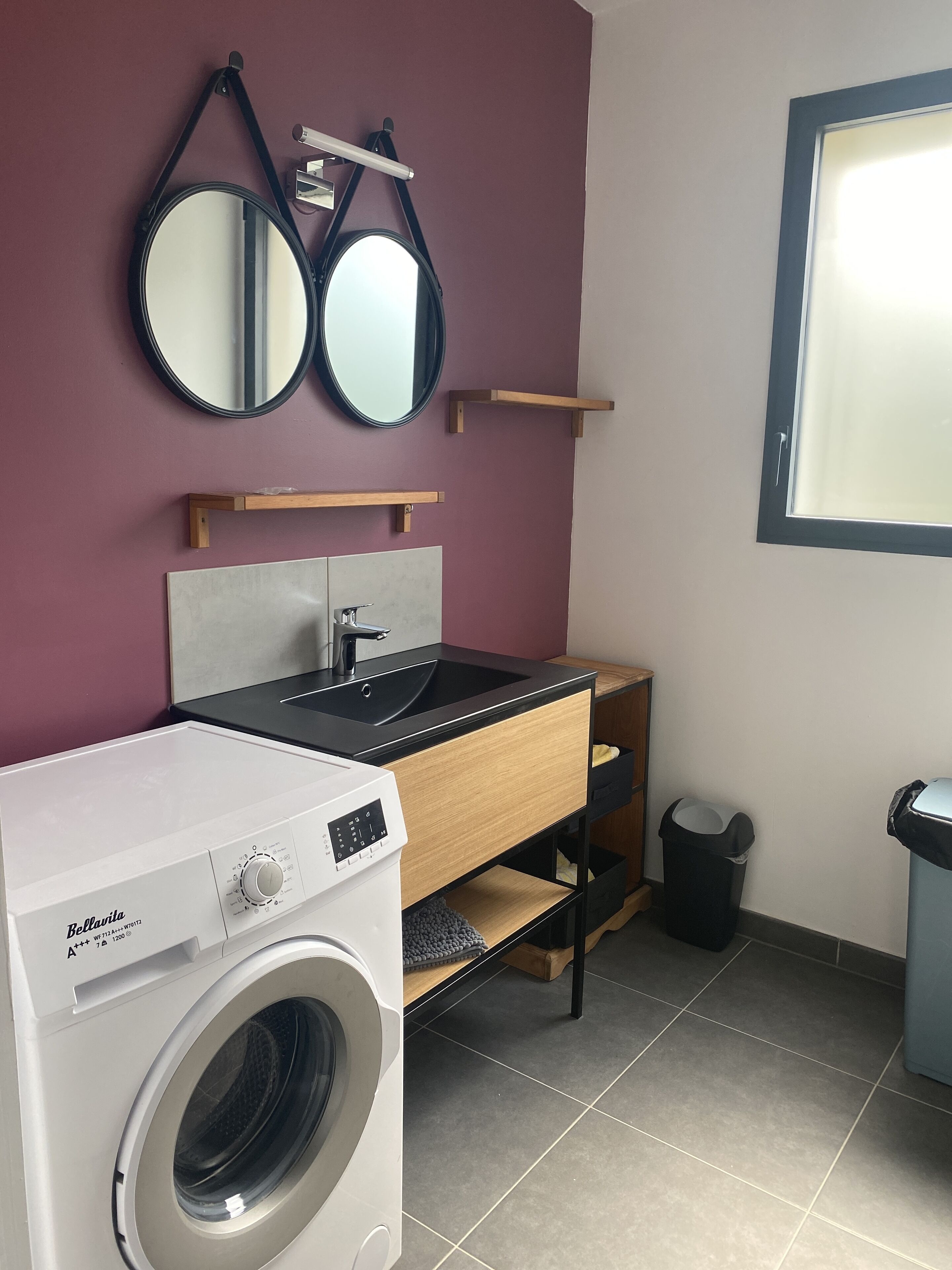 A compact bathroom with a washing machine, a sink, and two mirrors.