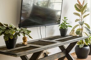 A wooden table with a TV mounted on the wall, surrounded by potted plants. - Stylish 2-Bedroom Green Oasis (Tel Aviv)