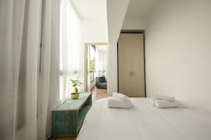 Un dormitorio con una cama, una ventana con cortinas, una mesita con una planta y un armario.