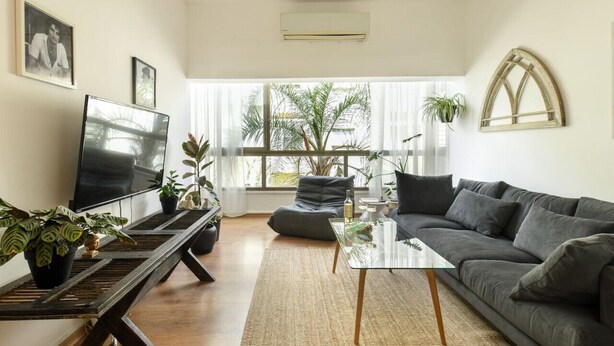 A modern living room with a sofa, a glass coffee table, a TV, and potted plants. - Stylish 2-Bedroom Green Oasis (Tel Aviv)