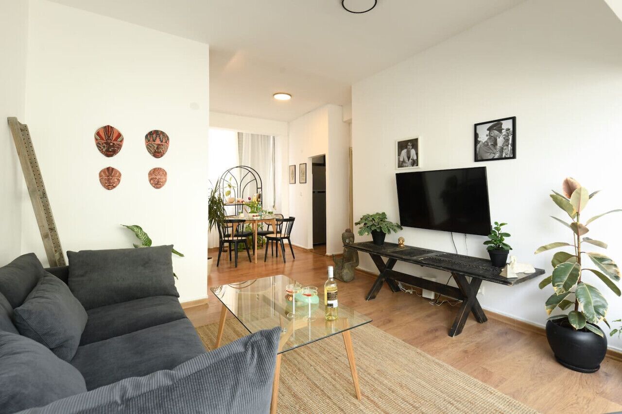 A modern living room with a sofa, a glass coffee table, a TV, and a dining area with a table and chairs.
