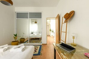 A hotel room with a bed, a desk with a laptop, a mirror, a door, and a small plant. - Stylish 2-Bedroom Green Oasis (Tel Aviv)