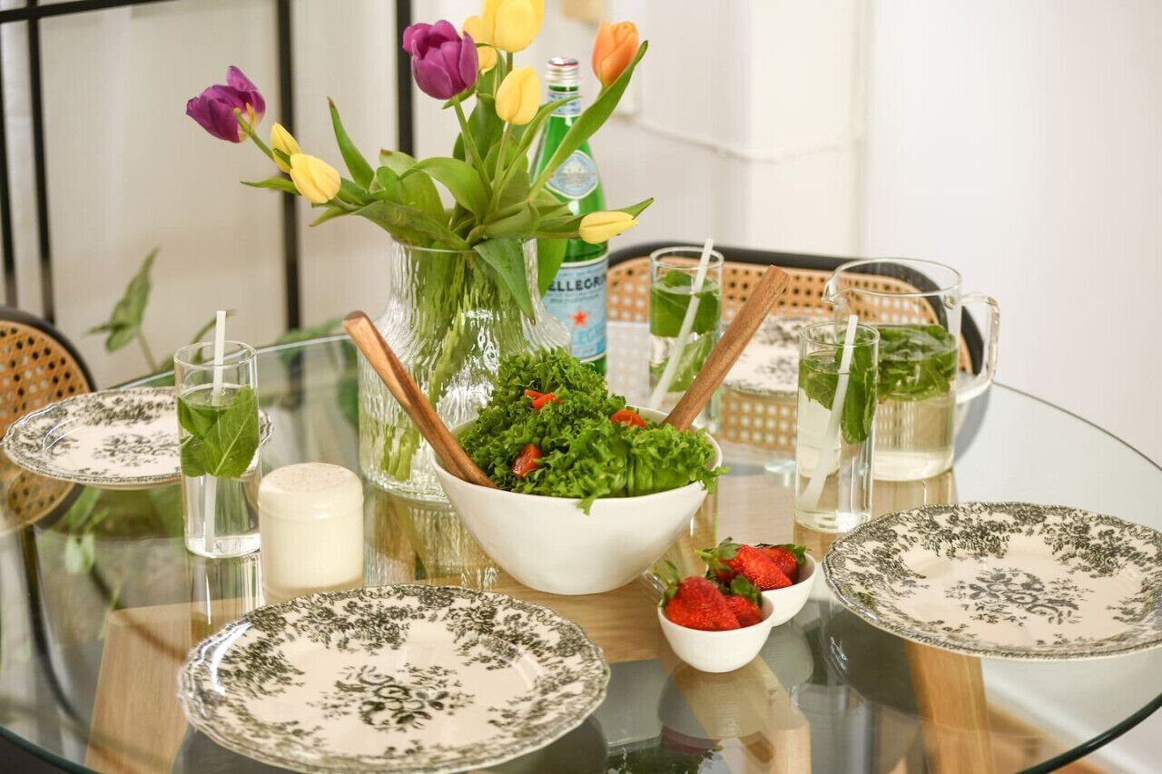 Une table en verre avec un saladier, une bouteille d’eau et un pichet de thé vert.
