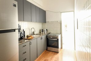 A compact kitchen with grey cabinets, a stainless steel stove, and a white tiled backsplash. - Stylish 2-Bedroom Green Oasis (Tel Aviv)