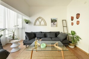 A modern living room with a dark grey sofa, a glass coffee table, and various plants. - Stylish 2-Bedroom Green Oasis (Tel Aviv)