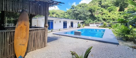 A pool area with a wooden deck, a surfboard, and a building with blue doors.